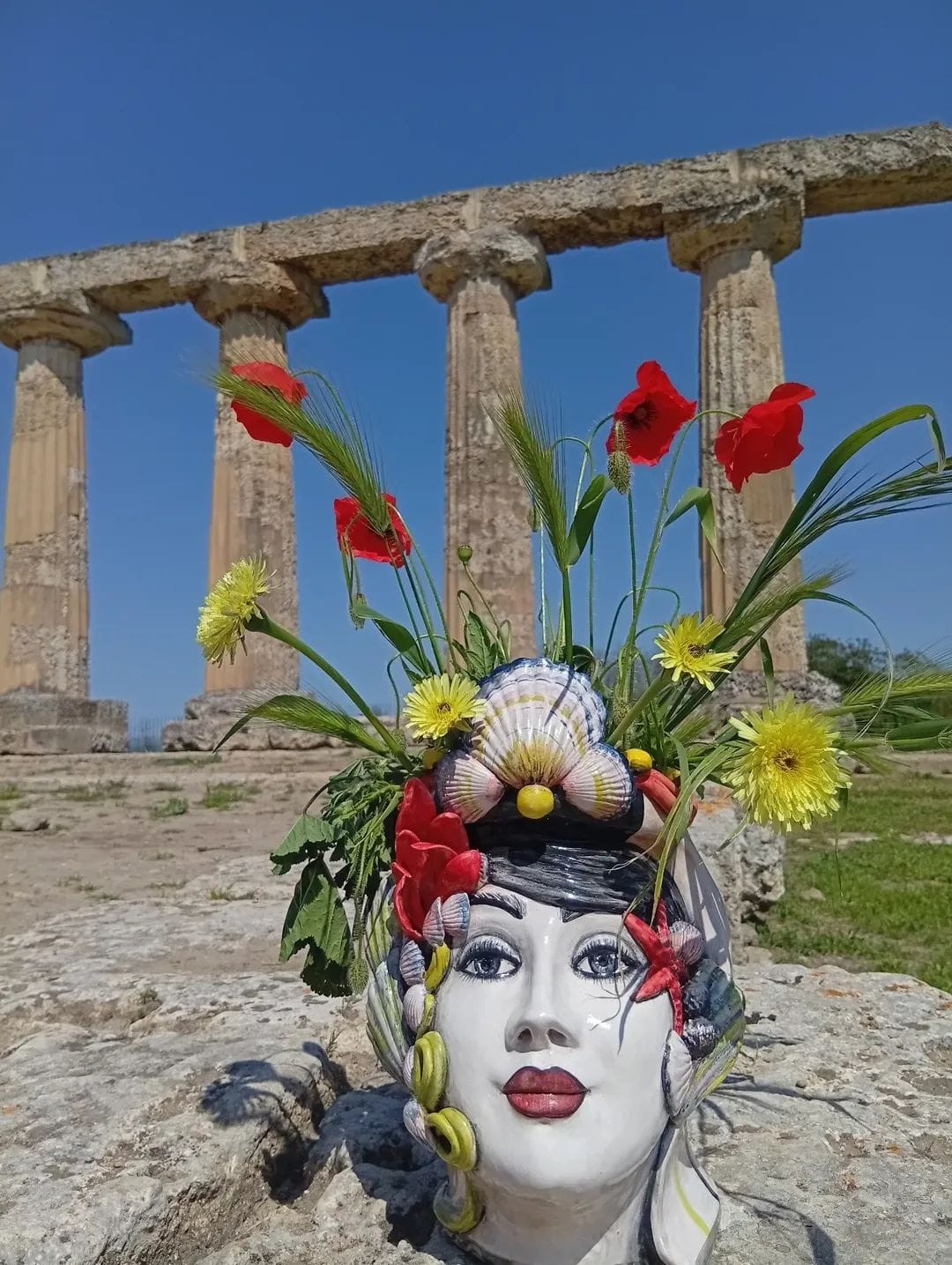 Scultura di volto femminile ornato fotografata davanti a colonne